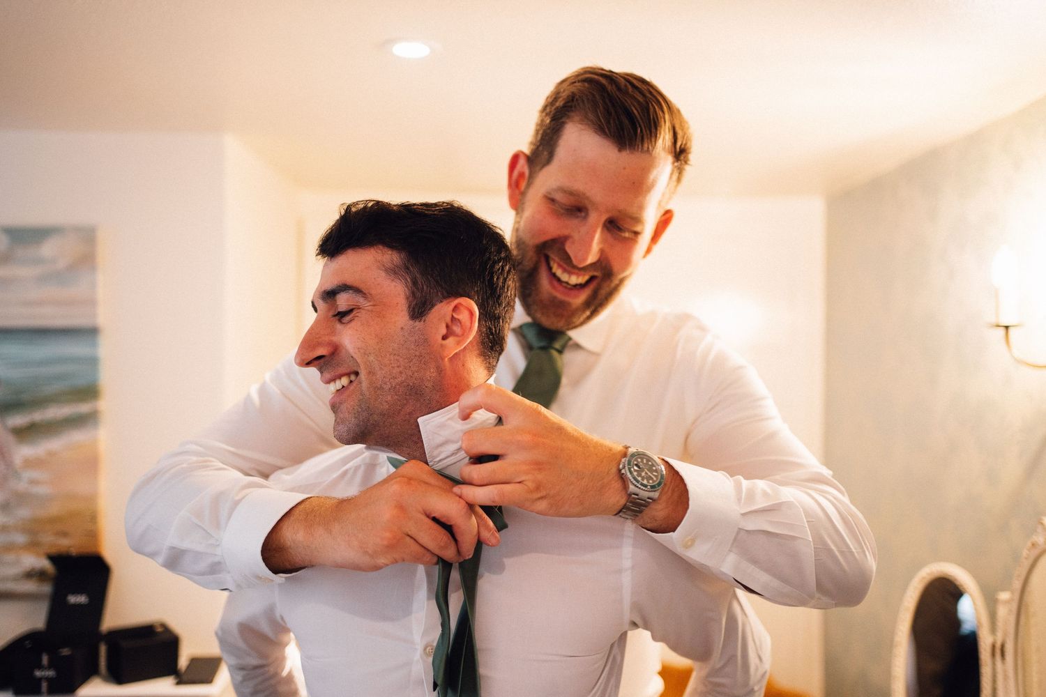 Two people sharing a joyful moment while getting dressed in formal attire.