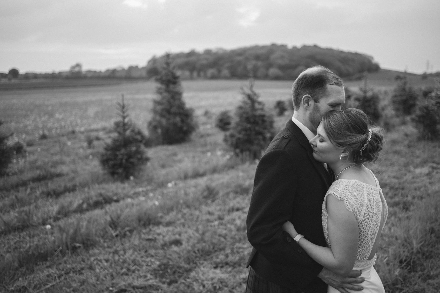Black and white photo of newlyweds walking through a scenic hillside landscape.
