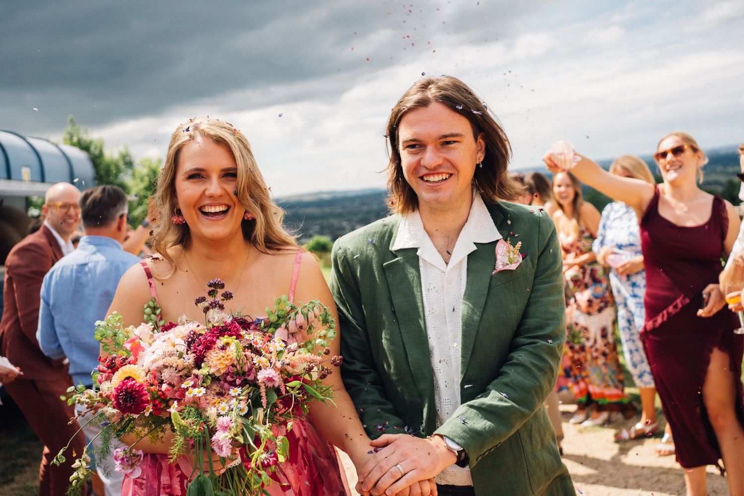 Wedding party celebrates outdoors with colorful floral bouquets and formal attire on a sunny day.