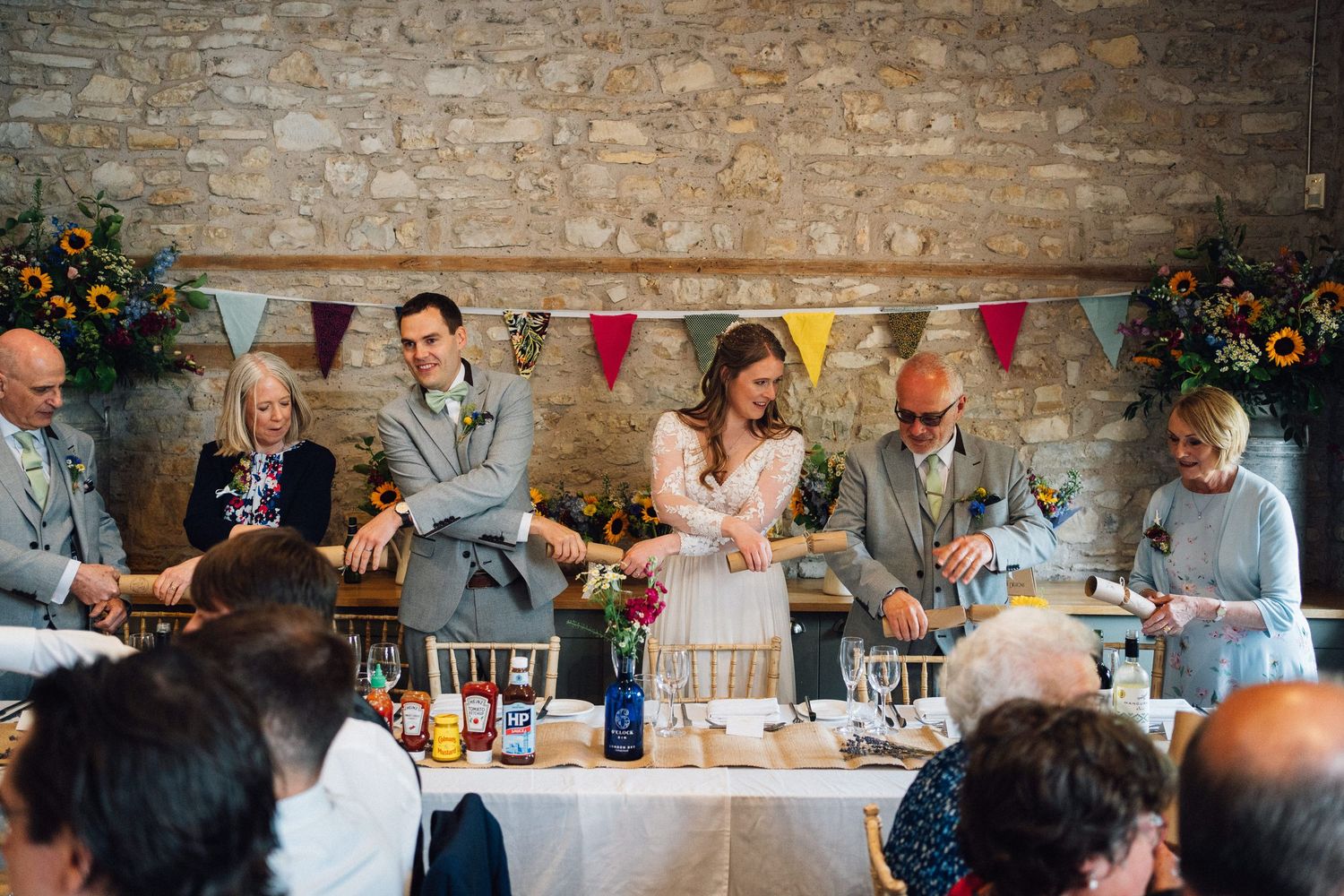 Wedding reception tables arranged along stone wall with festive bunting decorations.