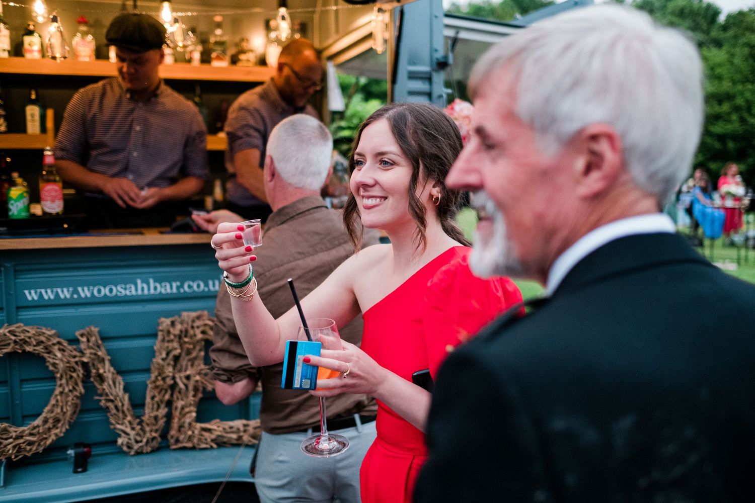 People socializing at an outdoor evening gathering with decorative lighting and rustic barn setting.