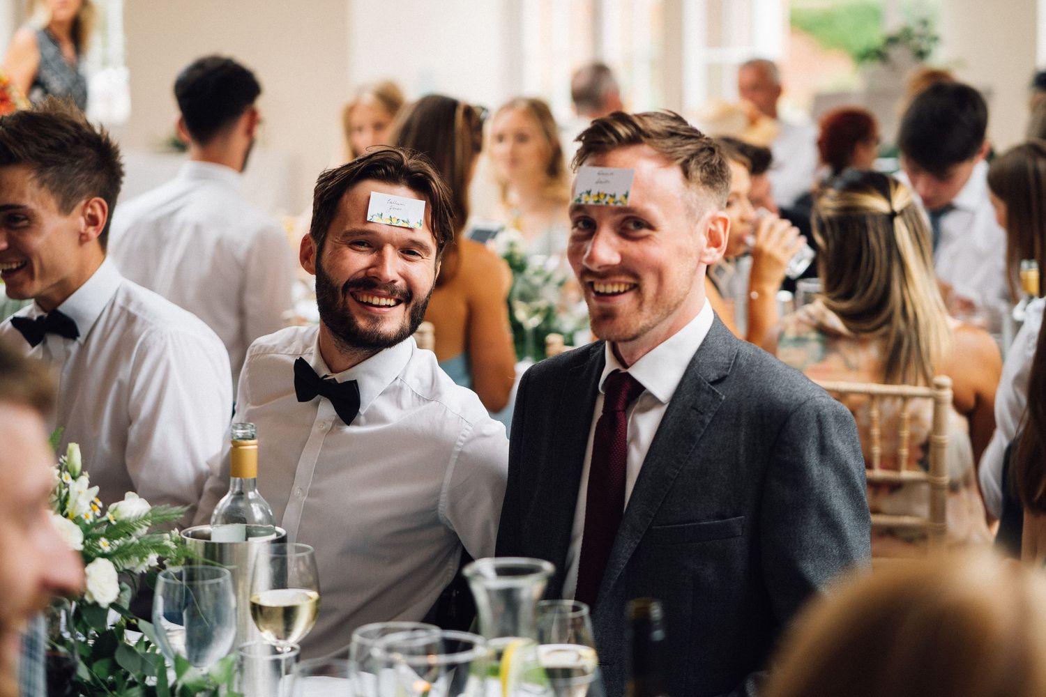 Wedding reception guests laugh and smile while seated at decorated dining tables.