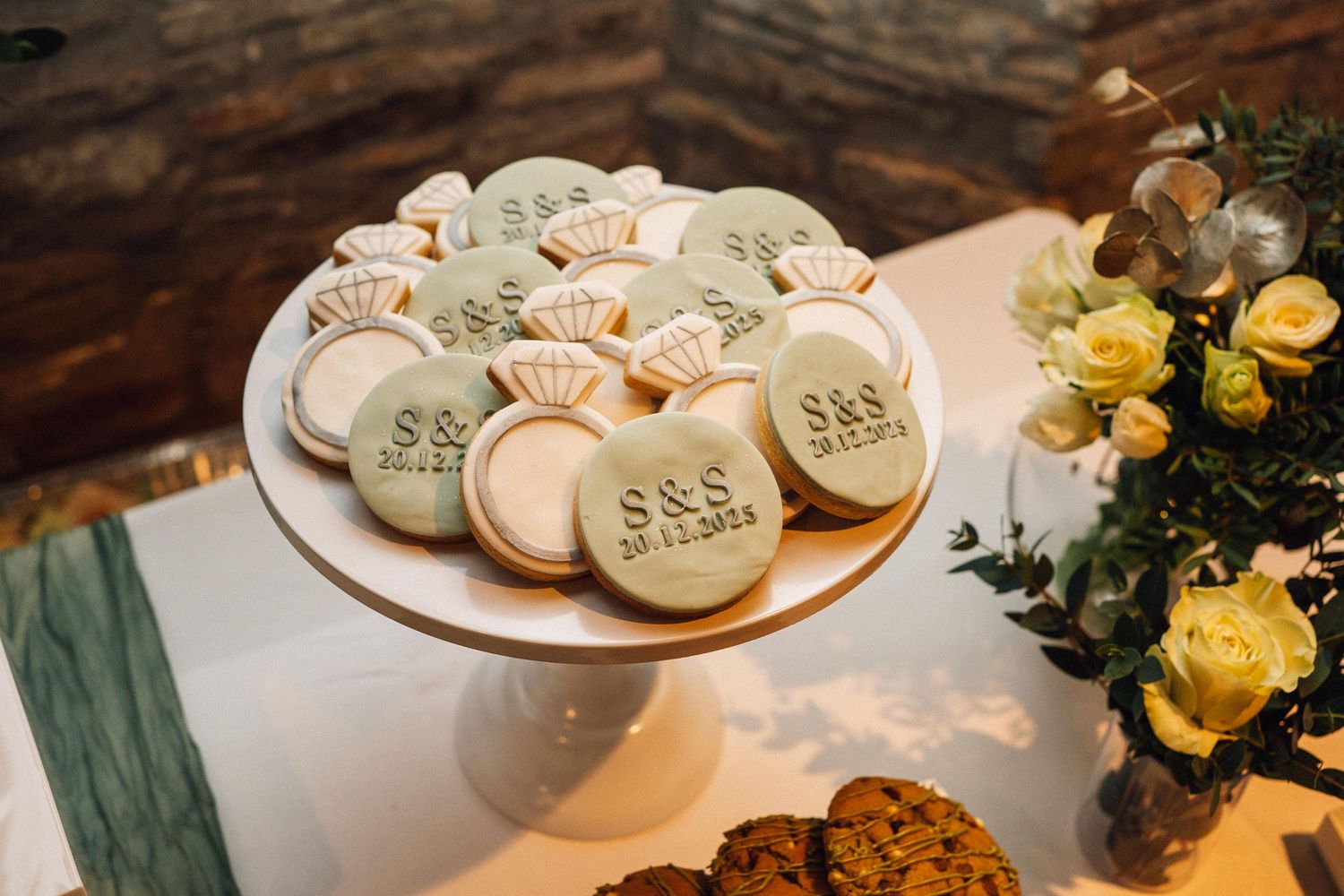 Wedding cookies and desserts displayed on white plates with yellow floral decorations.