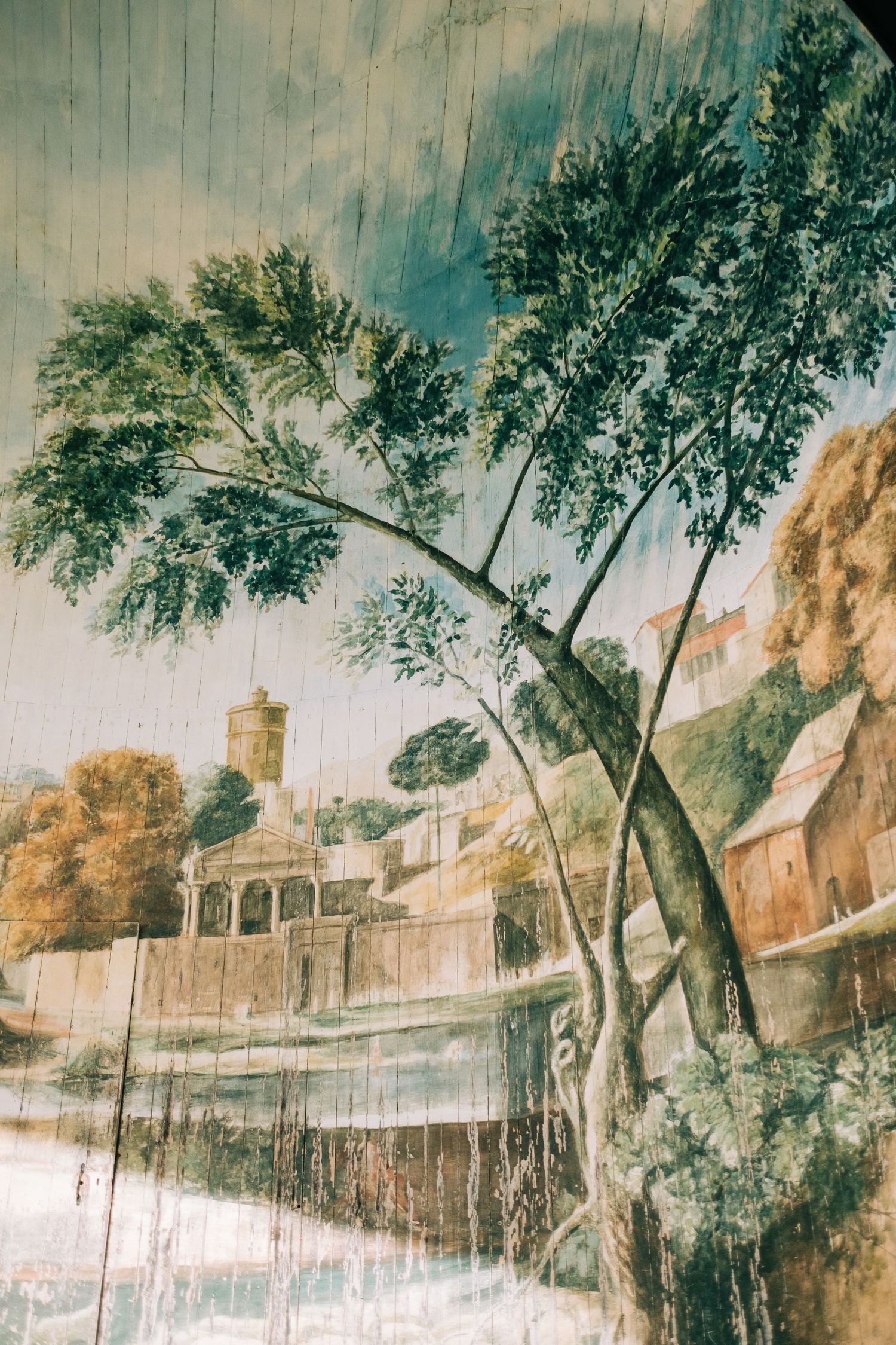 A vintage mural depicting a pastoral landscape with trees and buildings.