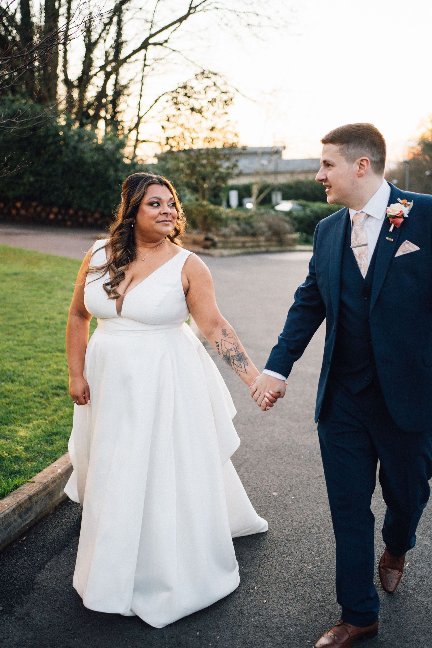 Couple walking hand in hand along an outdoor path during sunset.