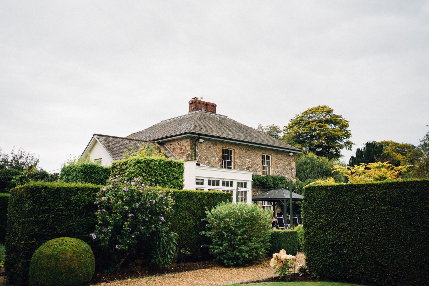 Panoramic view of a countryside wedding venue with manicured hedges and traditional brick buildings.