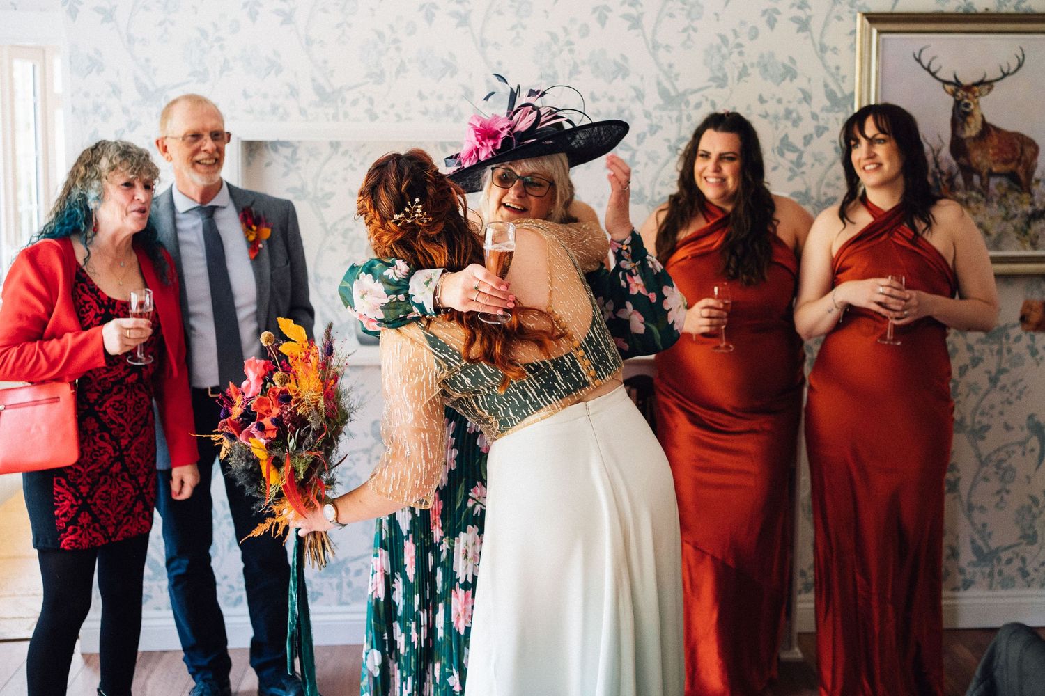 Wedding party members in burgundy dresses and formal attire pose together with floral arrangements at a celebration.