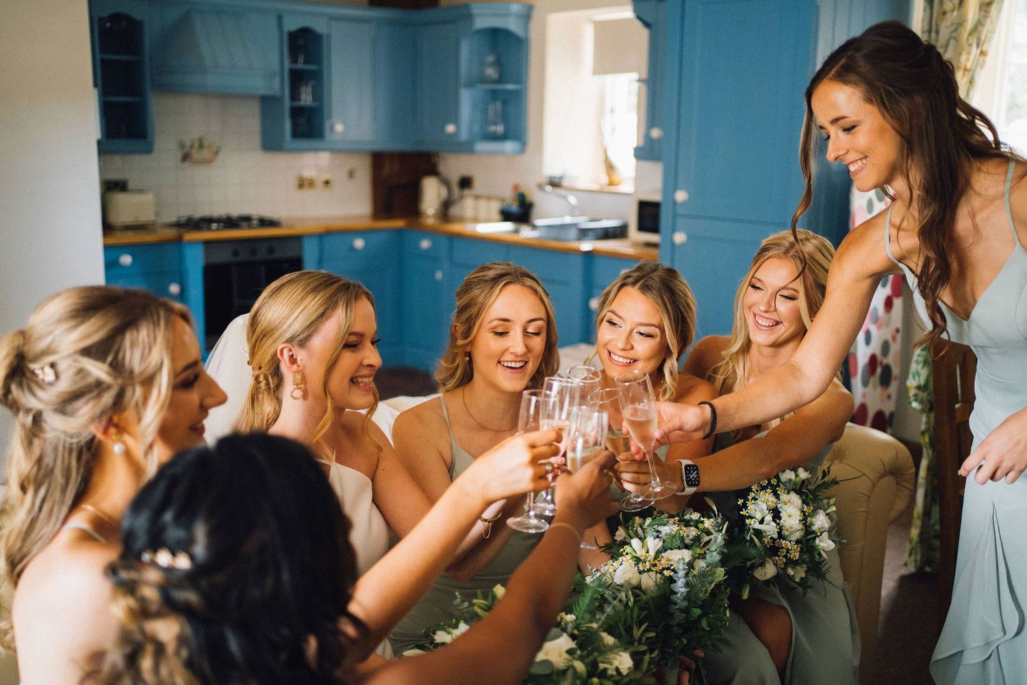 Bridesmaids and bride share an emotional moment while getting ready in a blue-walled room.