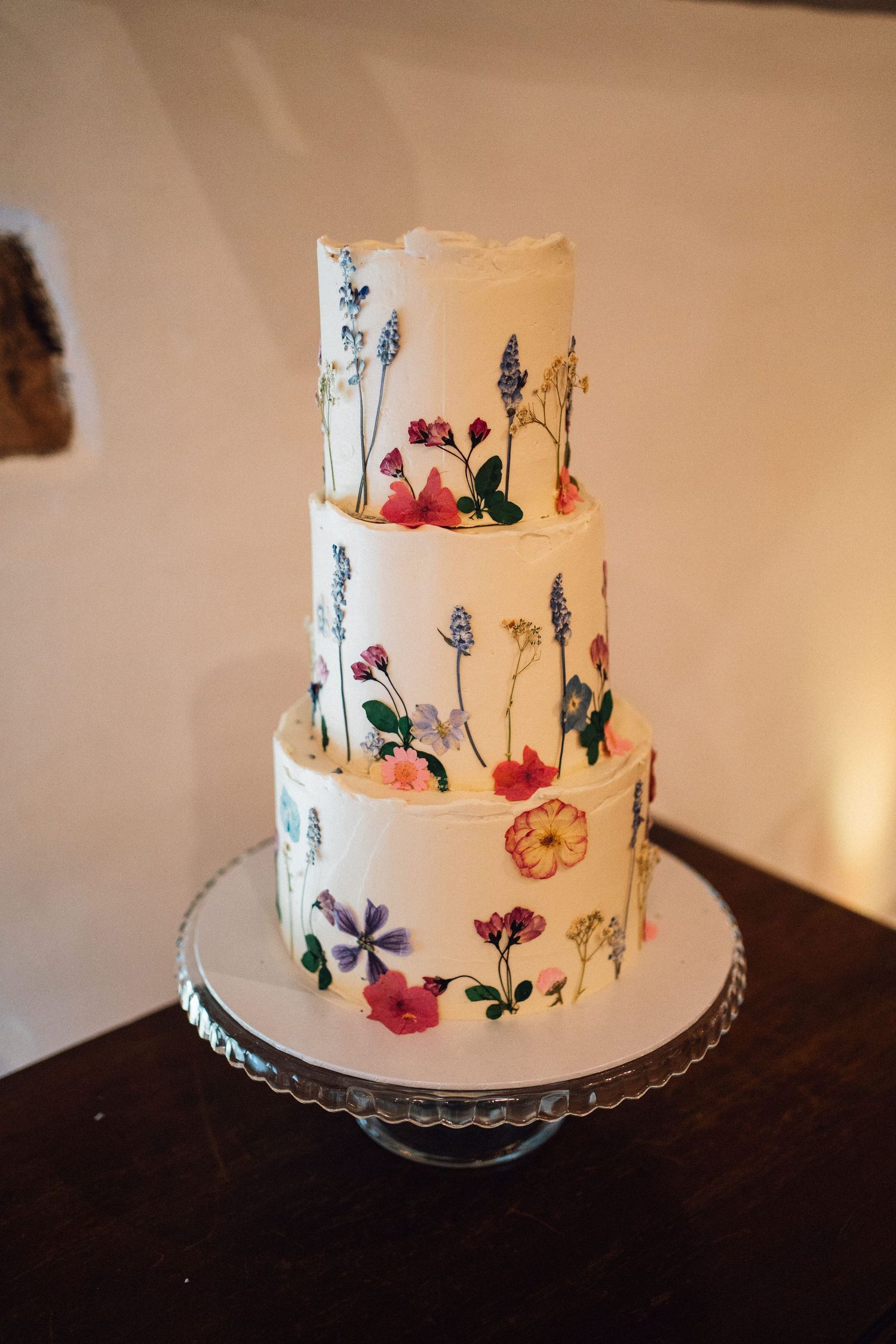 A white tiered wedding cake decorated with delicate hand-painted watercolor wildflowers and butterflies on display.