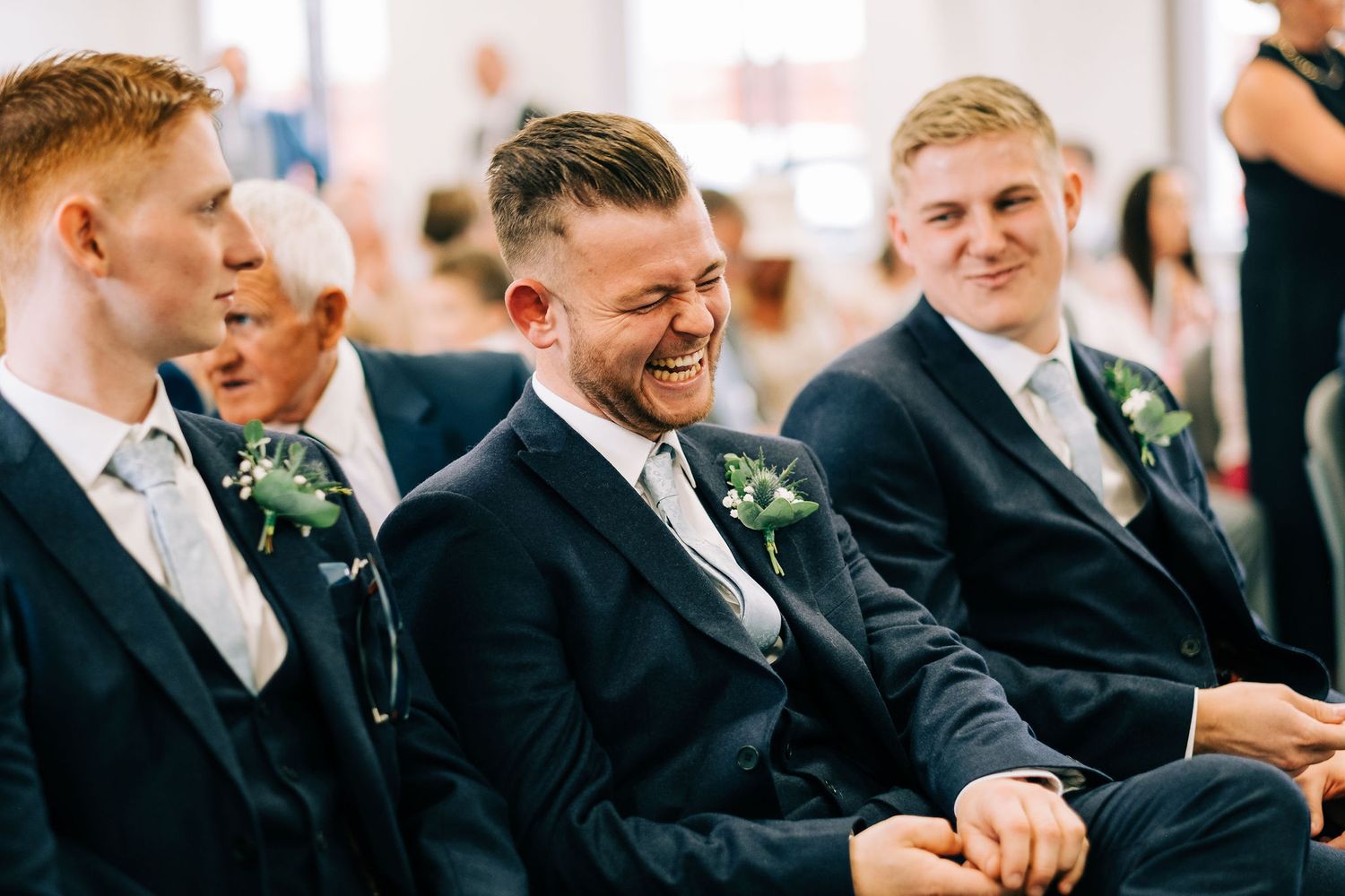 Groomsmen in navy suits share a lighthearted moment during the wedding ceremony.