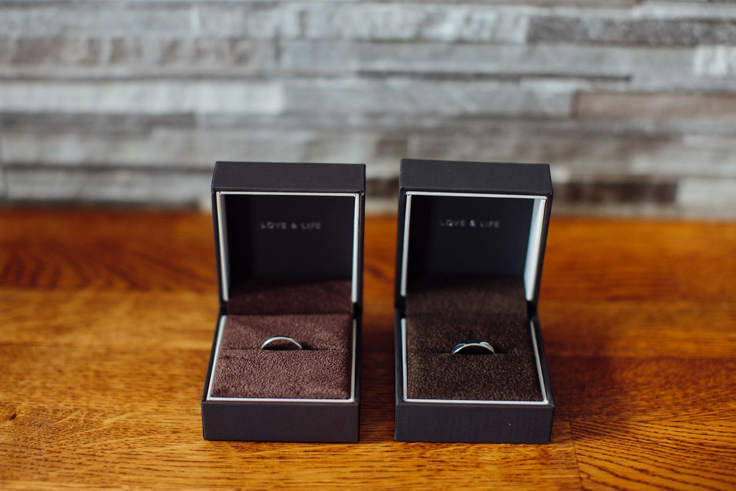 Wedding rings displayed in dark jewelry boxes on wooden surface.
