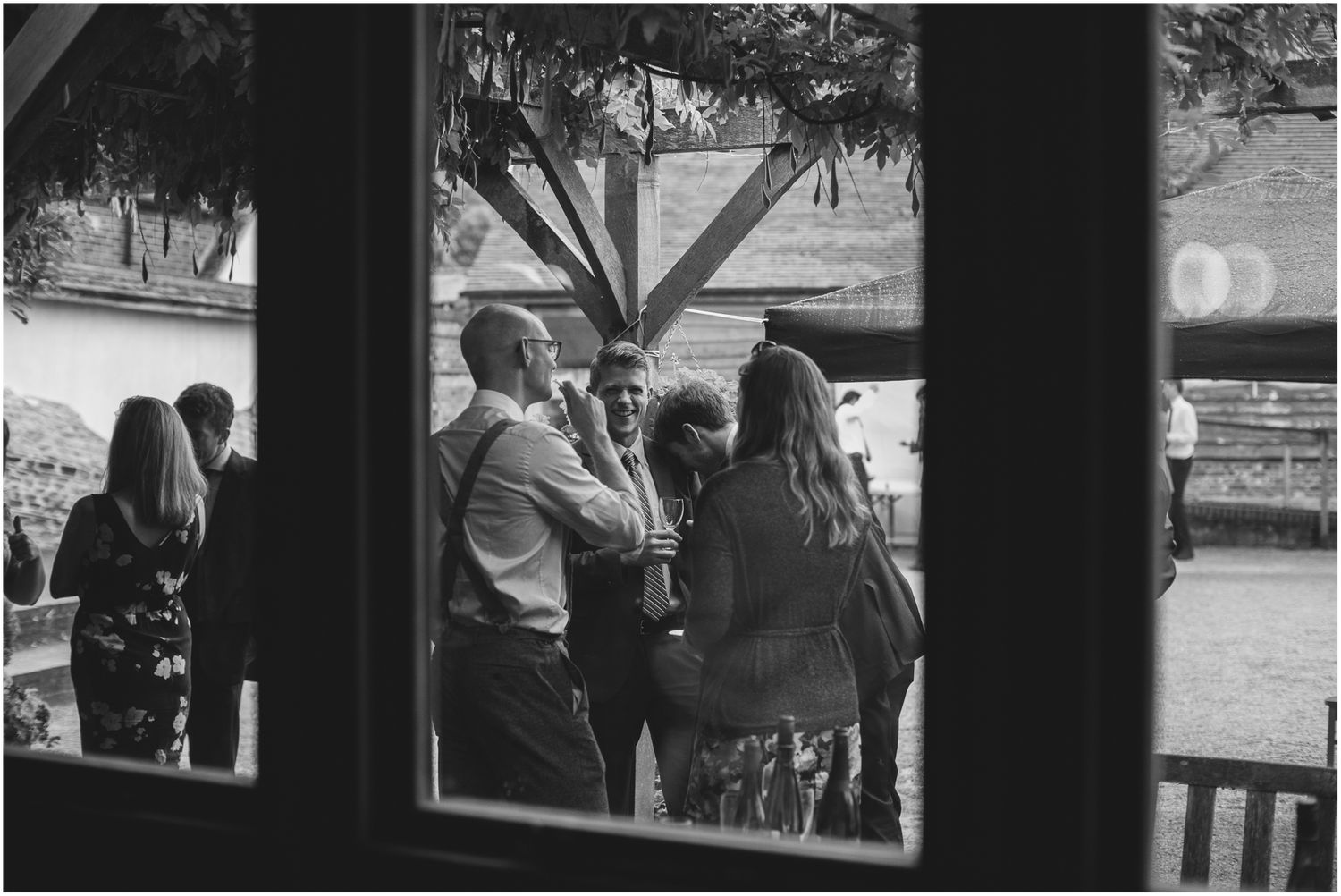 Black and white photograph of people gathered by large windows creating dramatic shadows.
