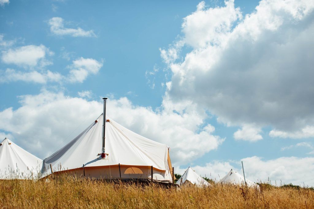 A white tent structure sits on a grassy hilltop against a bright blue sky with puffy white clouds.