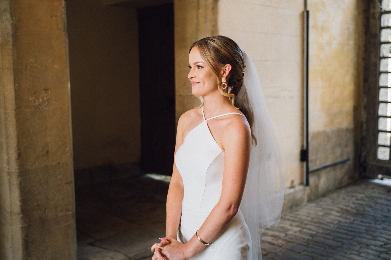A side profile portrait in warm lighting against a stone column background.
