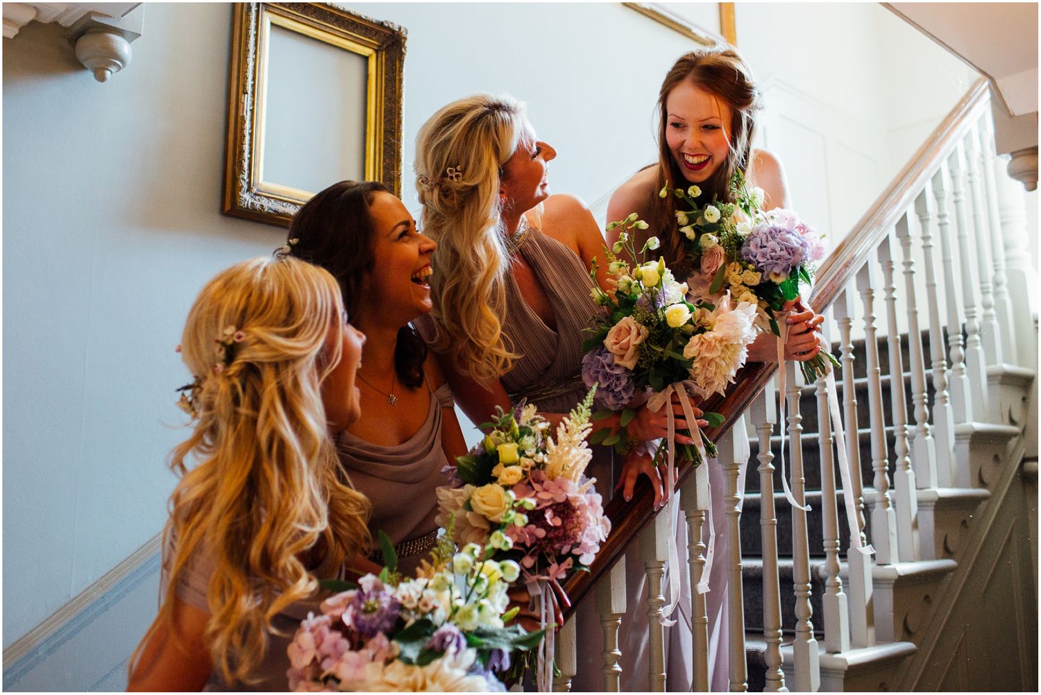 Bridesmaids sharing joyful moment on staircase while holding colorful bouquets.