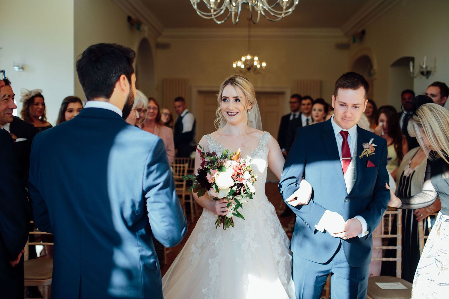 Elegant wedding ceremony taking place in a bright indoor venue with chandelier lighting.