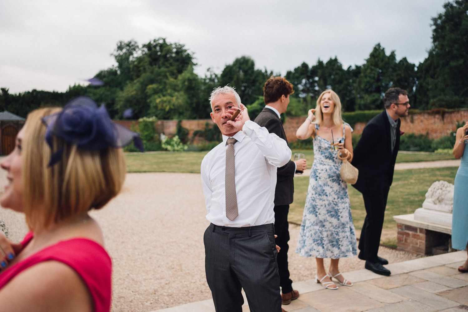 Guests gather at an outdoor wedding reception near stone benches.