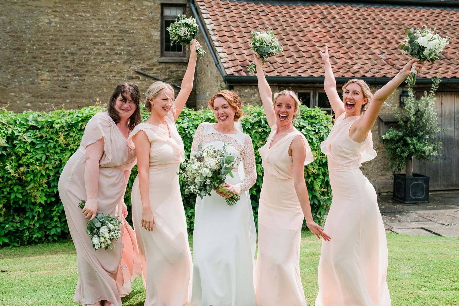 A group in white dresses poses together in a garden setting during a wedding celebration.