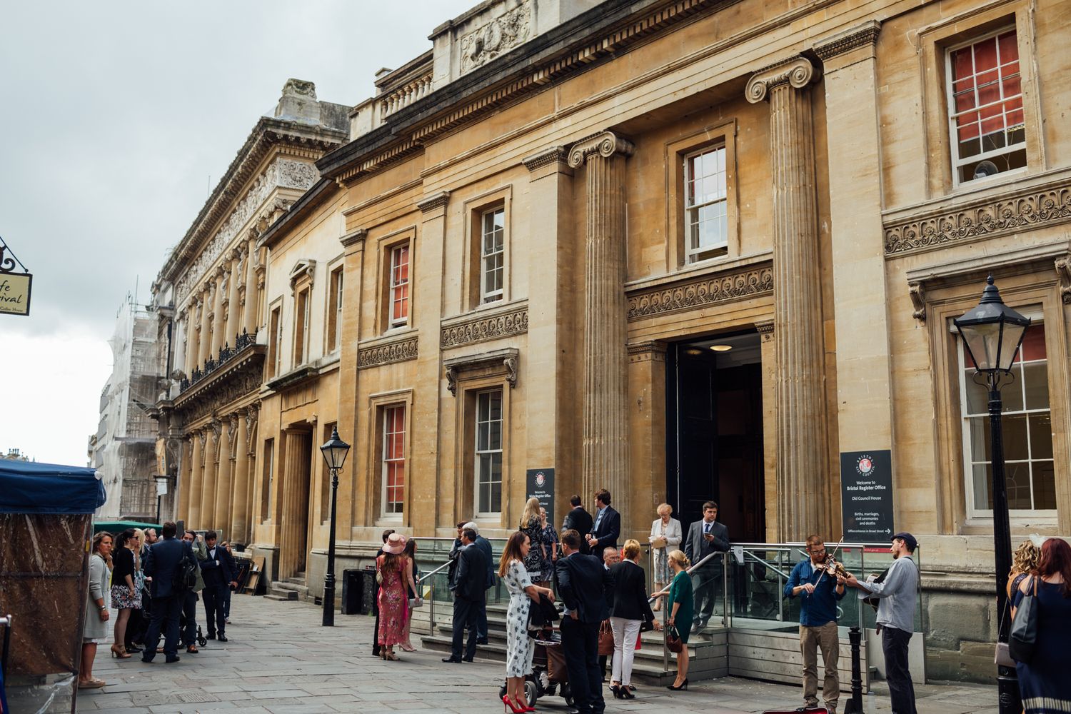 People wait in line outside historic Bath Assembly Rooms, a grand Georgian building with classical architecture.