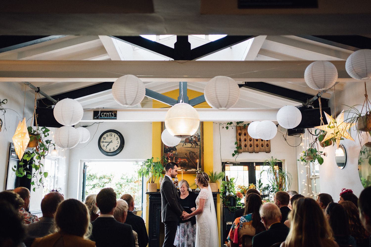 A wedding reception venue decorated with white paper lanterns and string lights hanging from the ceiling.