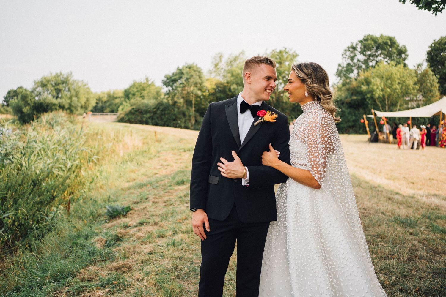 Marquee wedding in Taunton - A romantic couple shares an intimate moment together in a sunlit outdoor field during a formal celebration.