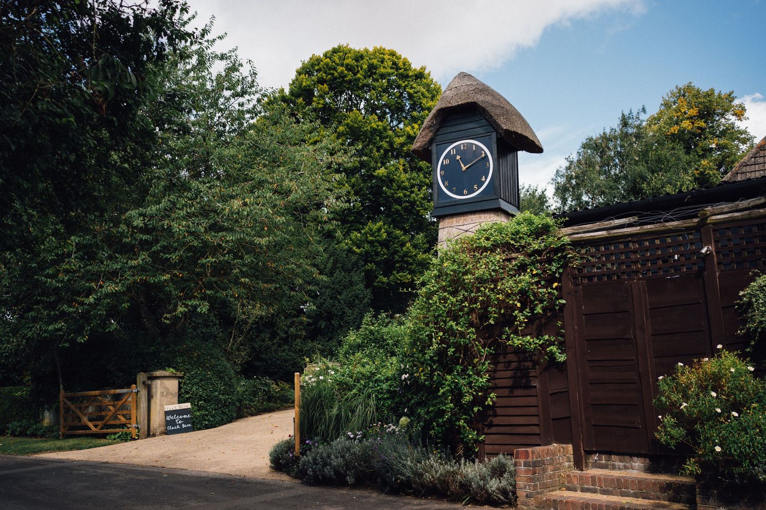 A scenic garden path leads to a wooden structure surrounded by lush greenery and trees on a sunny day.