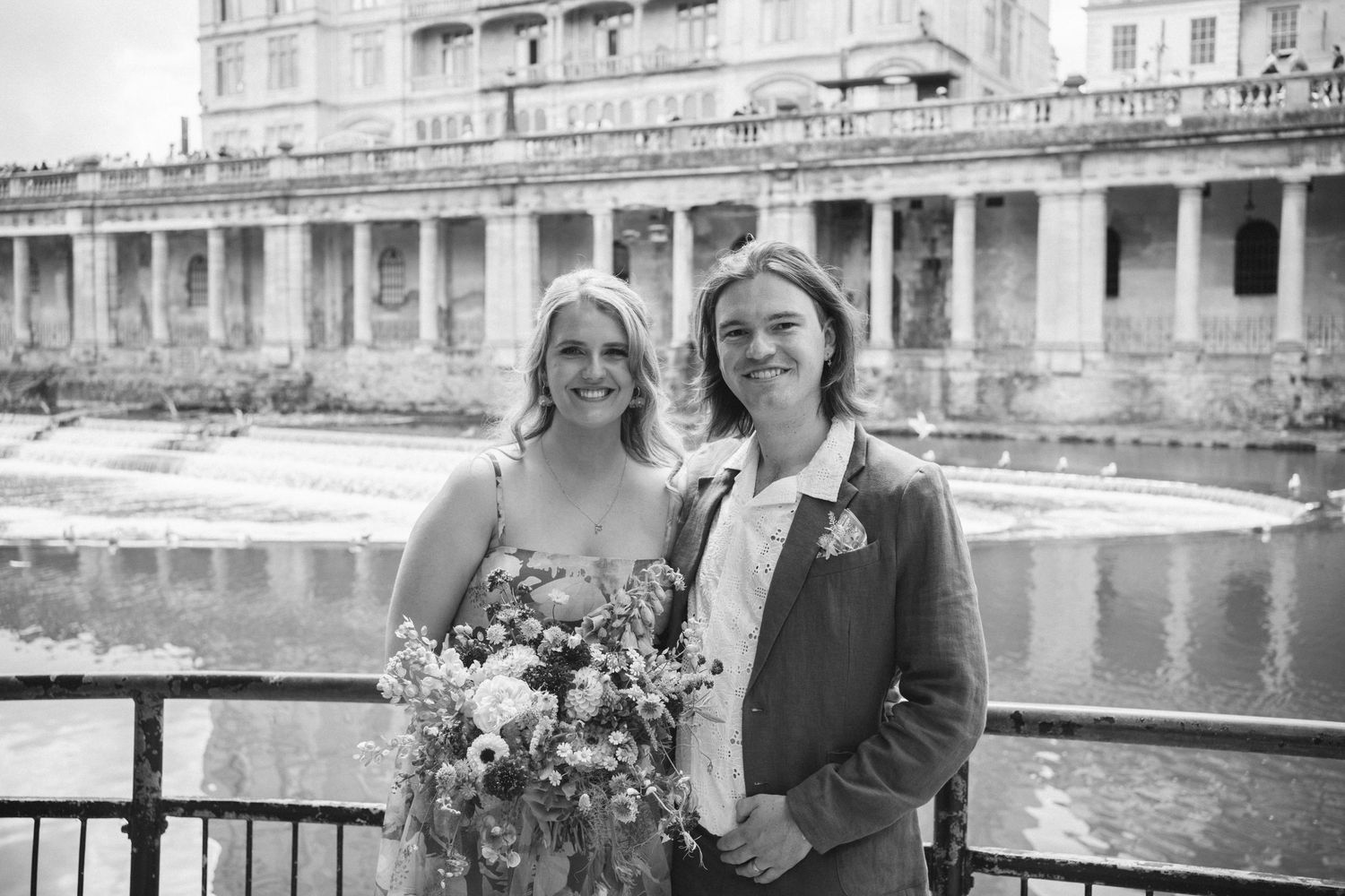 Black and white wedding portrait by historic stone architecture and water.