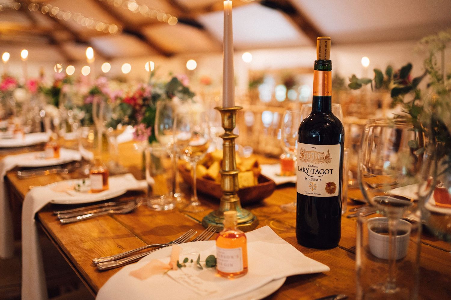 Wine bottles and elegant table decorations on wooden reception tables with warm lighting.