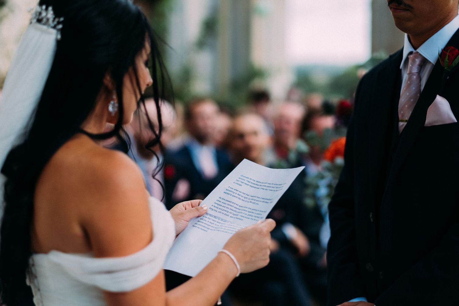 A couple reading their vows during an outdoor wedding ceremony with guests watching.