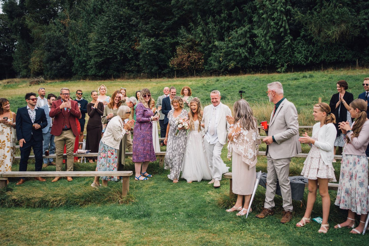 Wedding guests line up outdoors wearing summer attire and floral dresses.