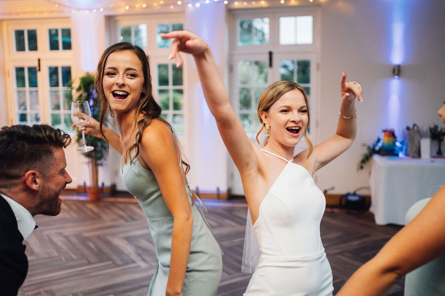 Wedding reception guests dancing energetically under indoor lighting at evening celebration.