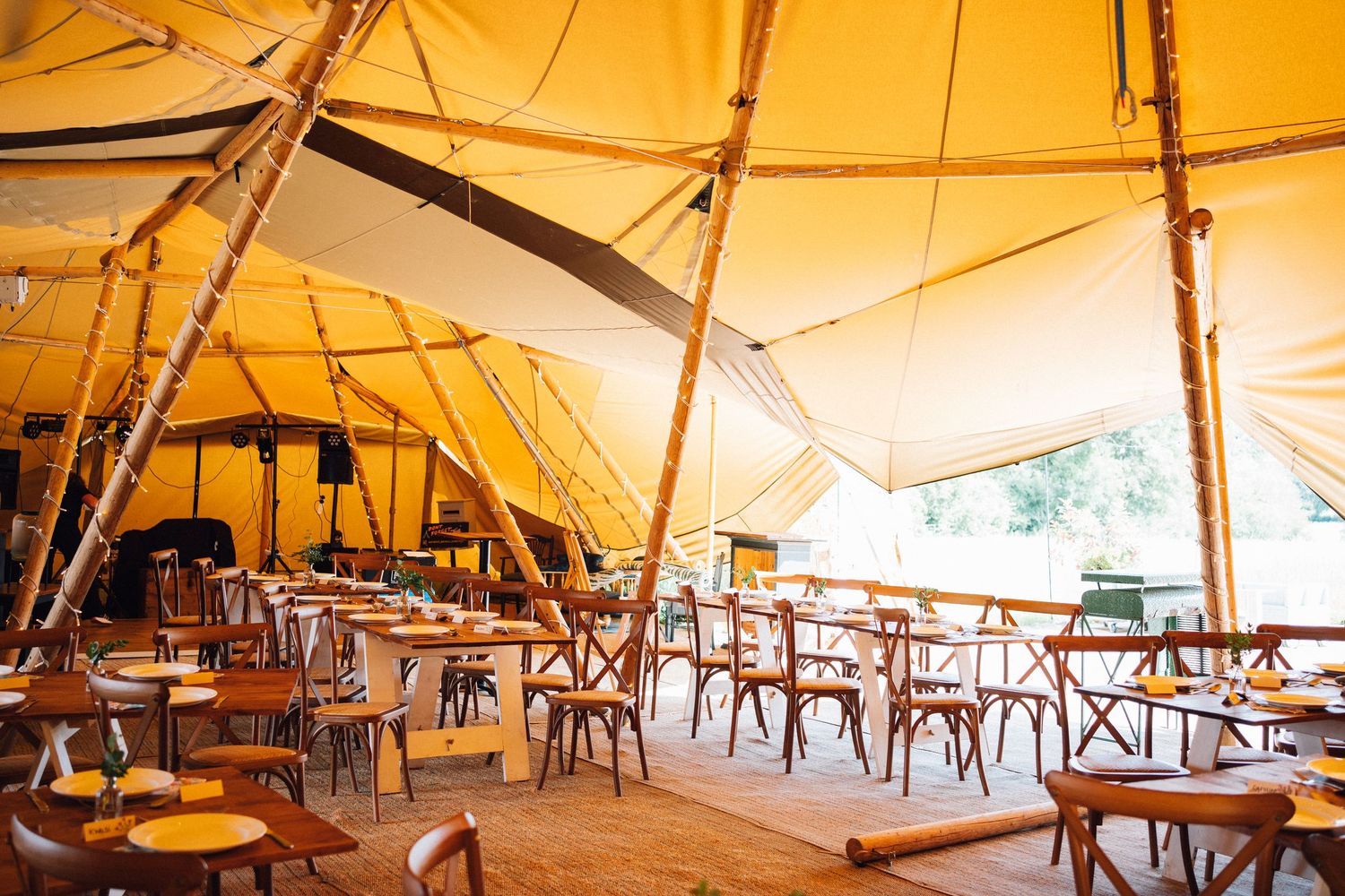 Interior view of a large event tent with wooden tables and chairs set up under warm lighting and canvas ceiling.