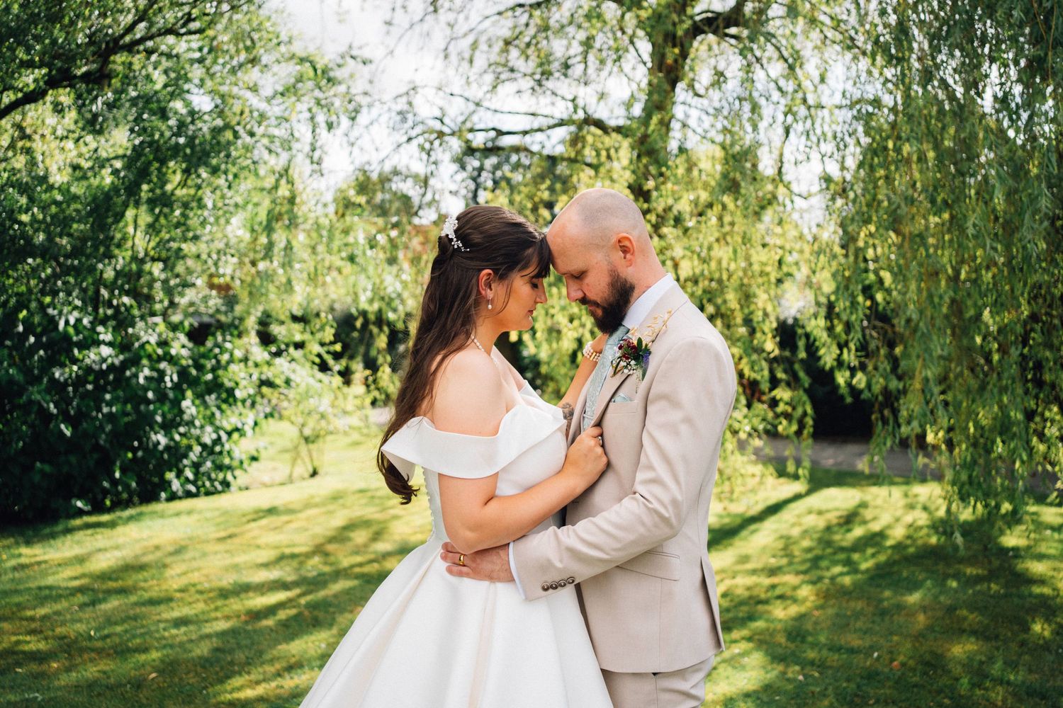 Couple sharing a romantic moment under weeping willow trees in a garden setting.
