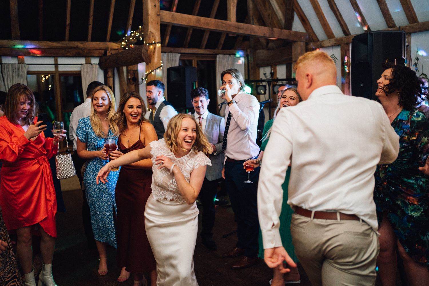 Wedding guests dancing and celebrating on a dimly lit dance floor during an evening reception.