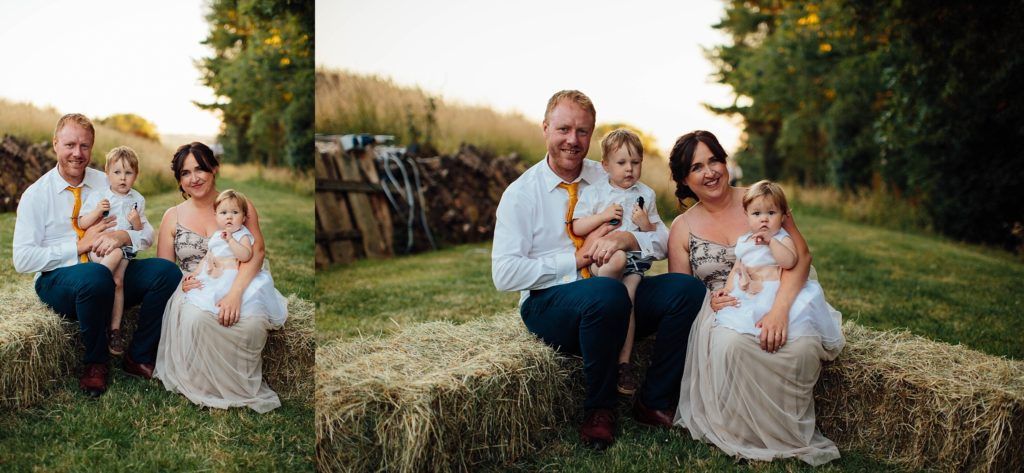 Family poses together on rustic hay bales during golden hour outdoor photo session.