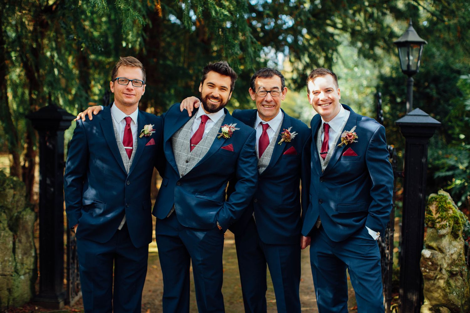Wedding party in coordinated navy suits posing together in a garden setting.