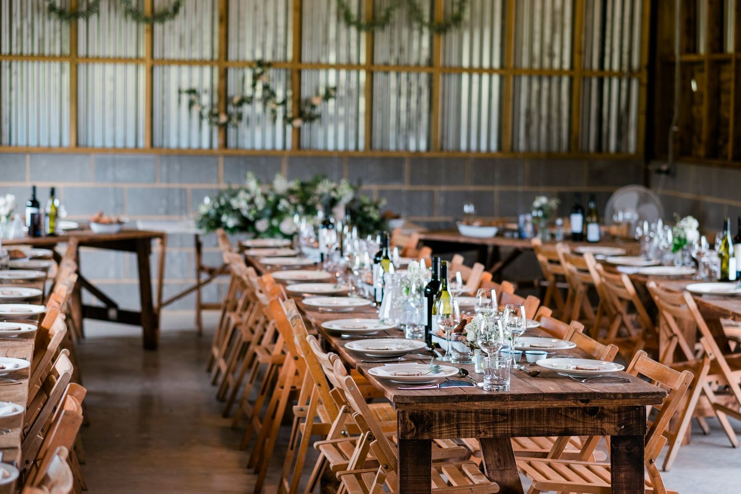 Long wooden tables with place settings arranged in a rustic barn venue with string lights overhead.
