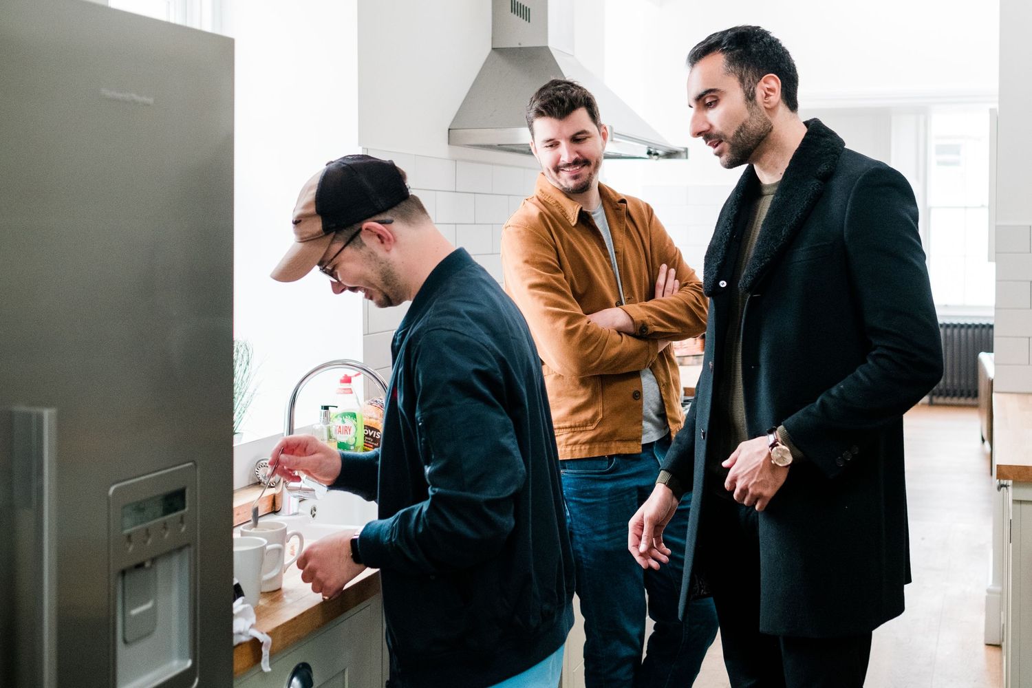 Three friends gathered in a modern kitchen having a casual conversation.