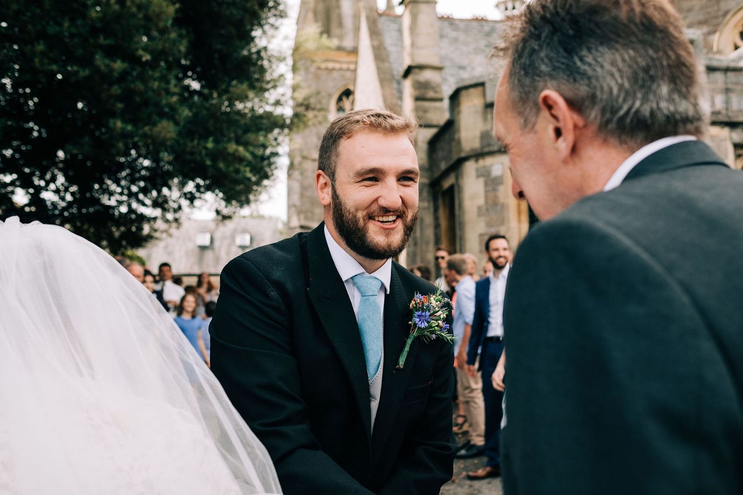 Wedding party gathered outside a historic church on a sunny day.