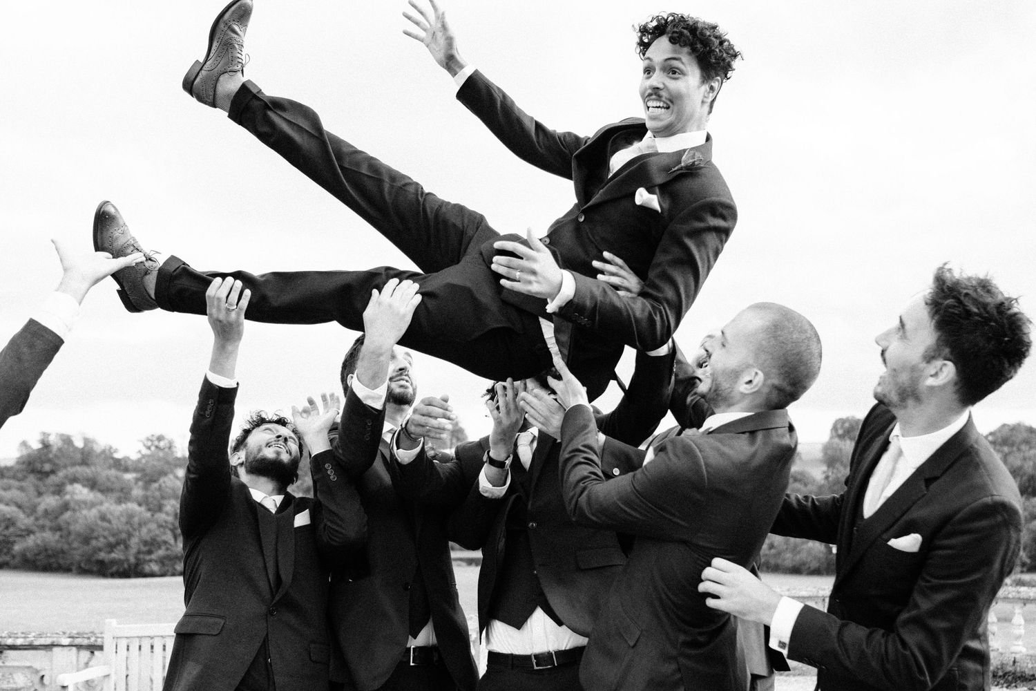 Black and white photo of wedding party jumping with arms raised in celebration.