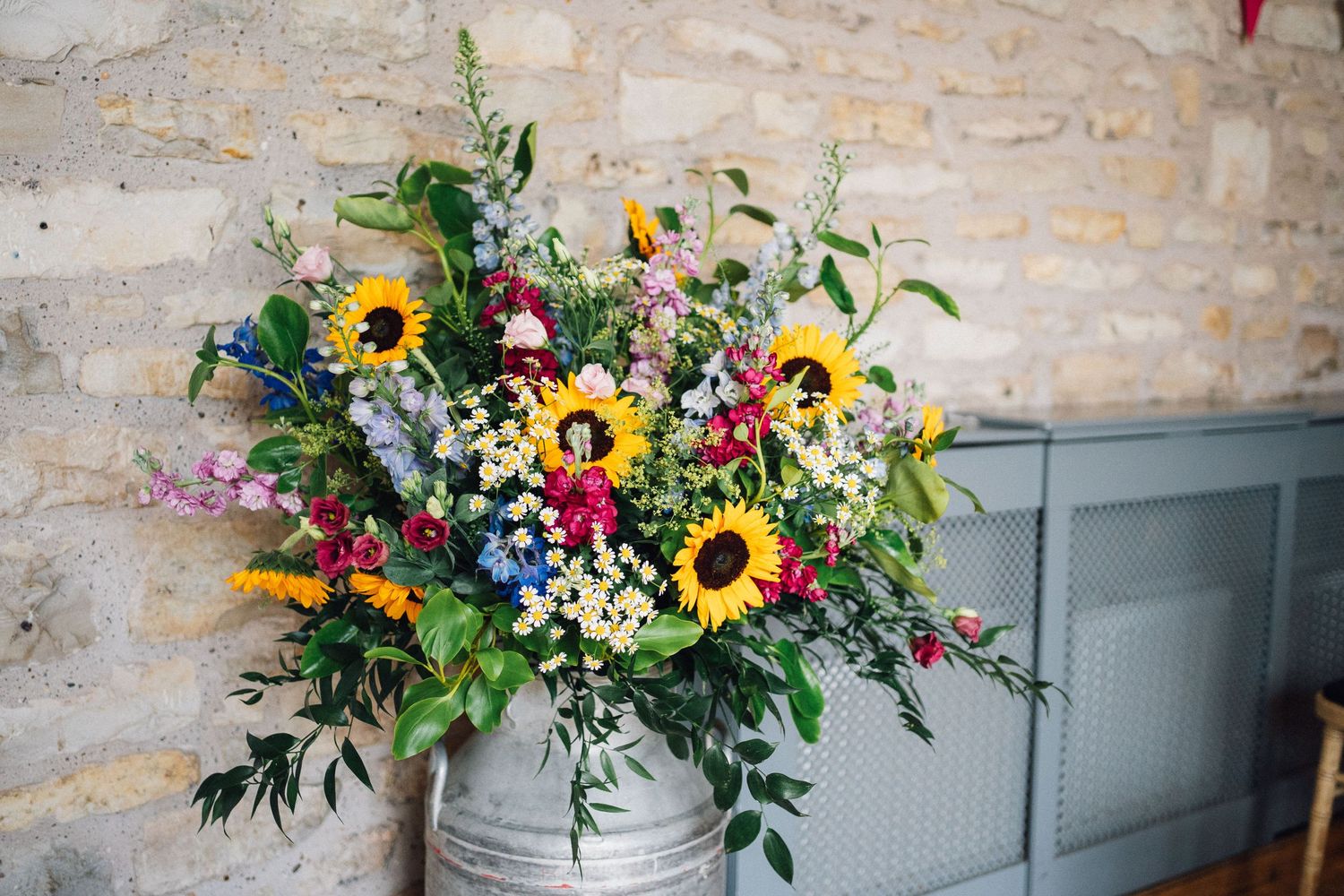 Vibrant wedding floral arrangements with sunflowers and wildflowers displayed against stone wall.