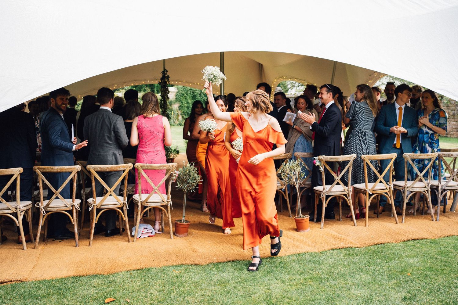 Wedding guests watch from their seats as celebrations unfold under a large outdoor tent.
