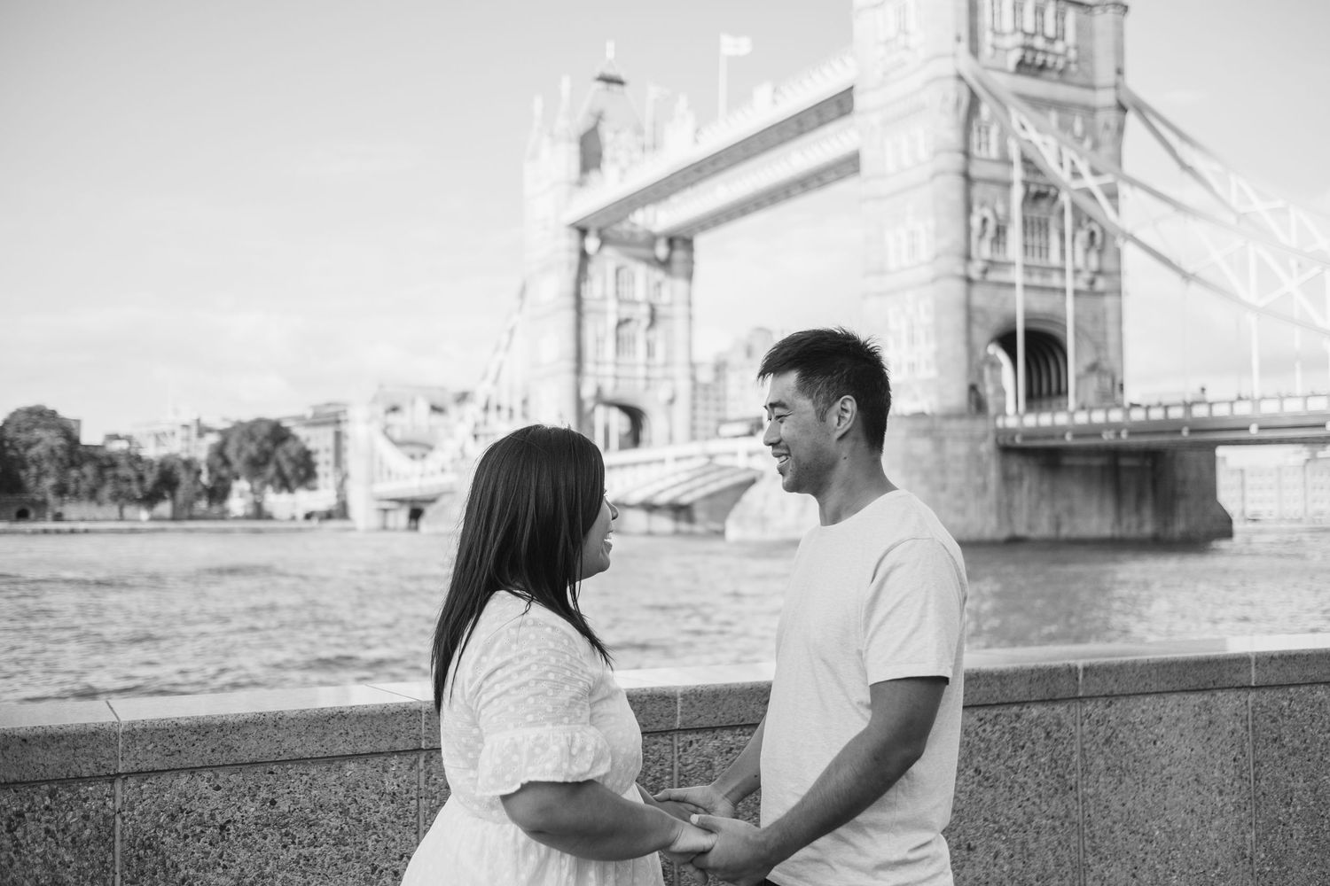 Black and white photo of Tower Bridge in London with people walking along the riverfront.