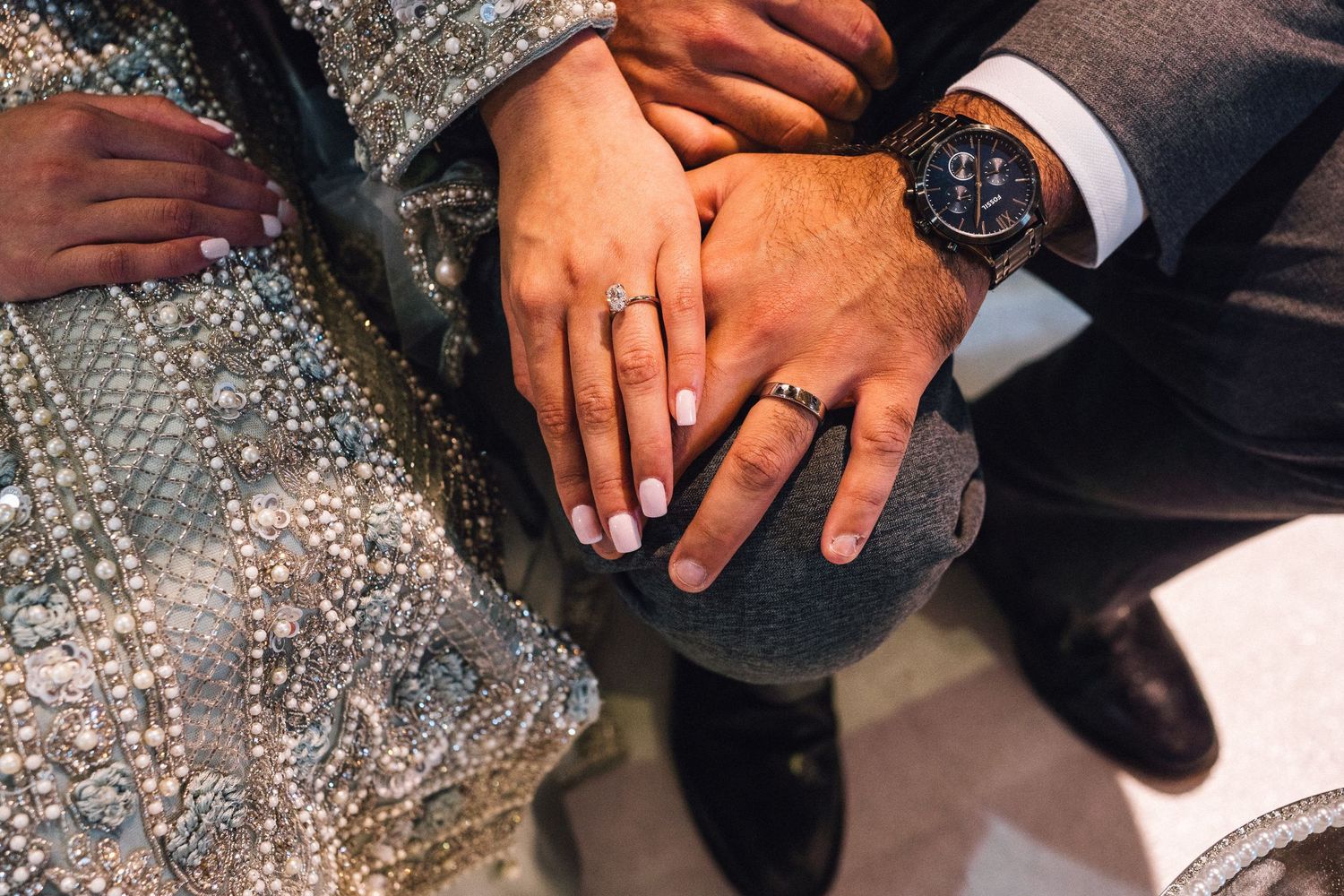 Close-up of hands showing wedding rings against sparkly formal attire.