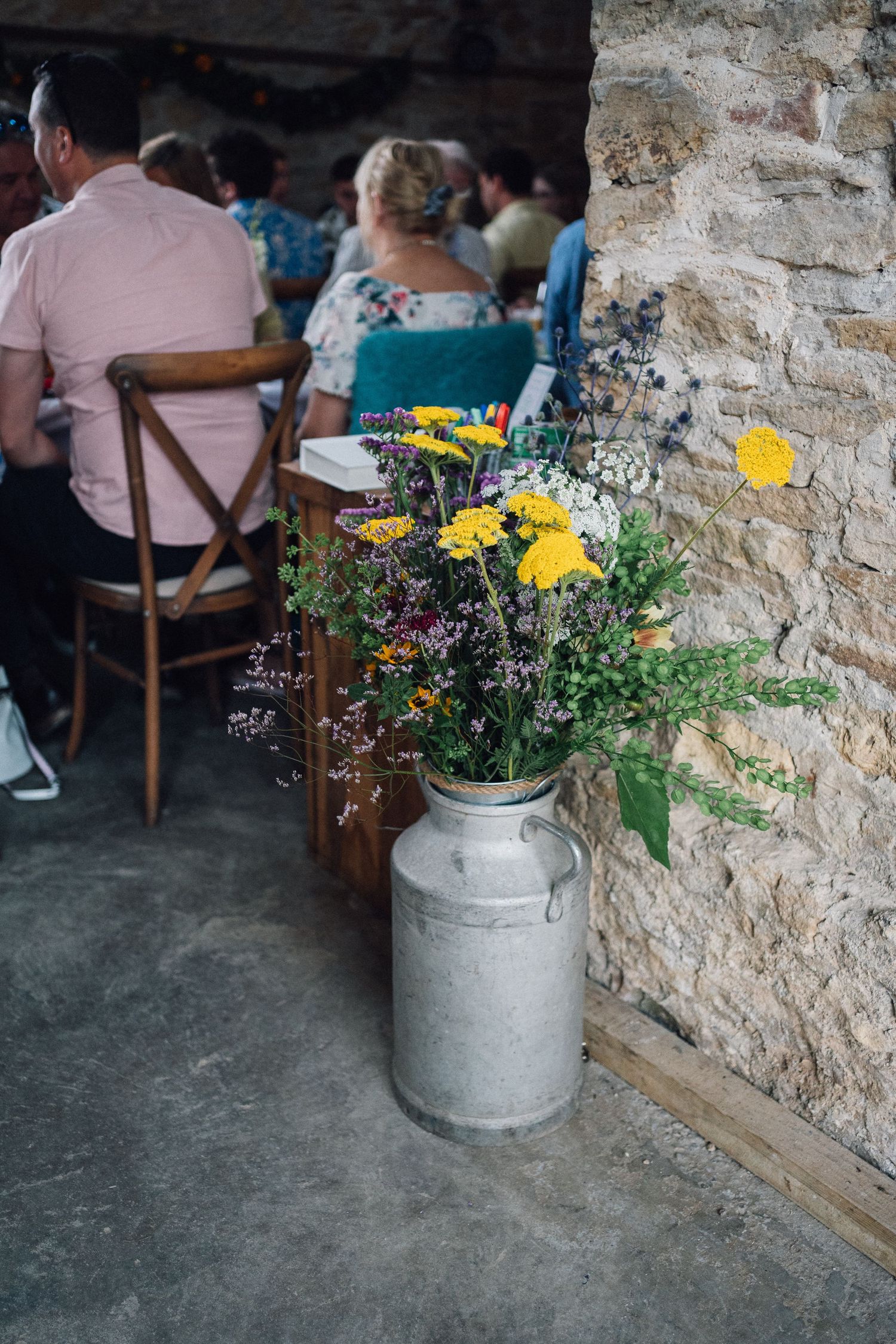 Rustic stone wall interior with yellow wildflowers in milk churn vases.