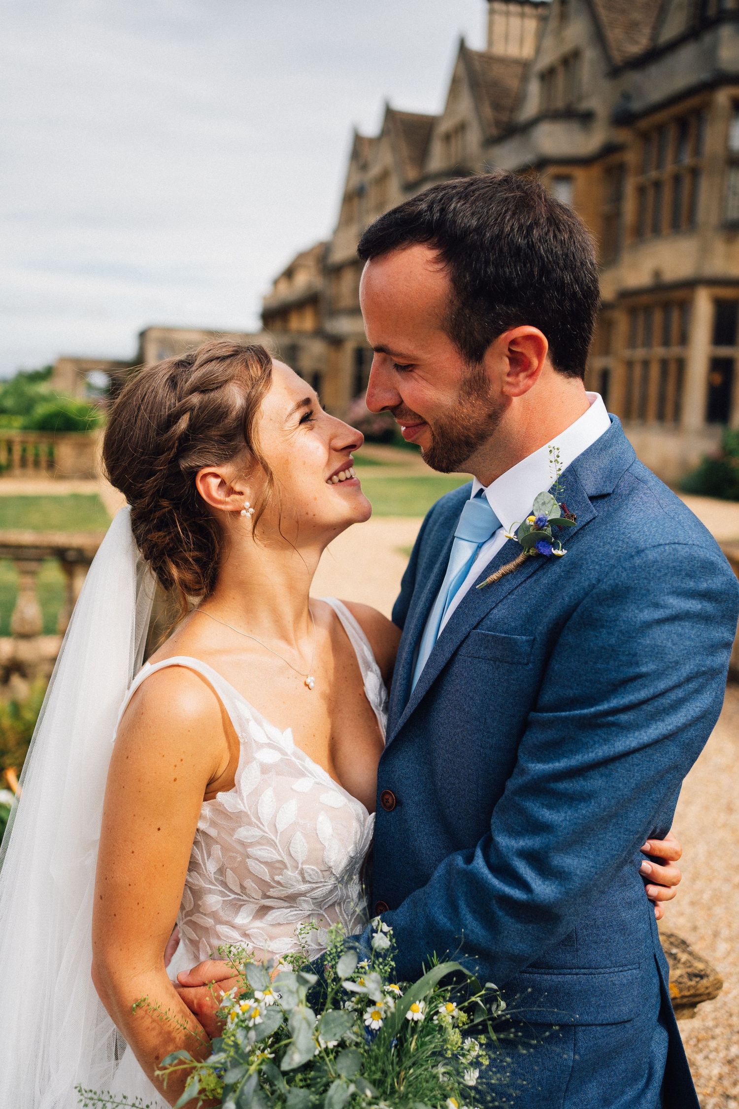 A romantic wedding portrait of a couple sharing a joyful moment against a historic stone building backdrop.