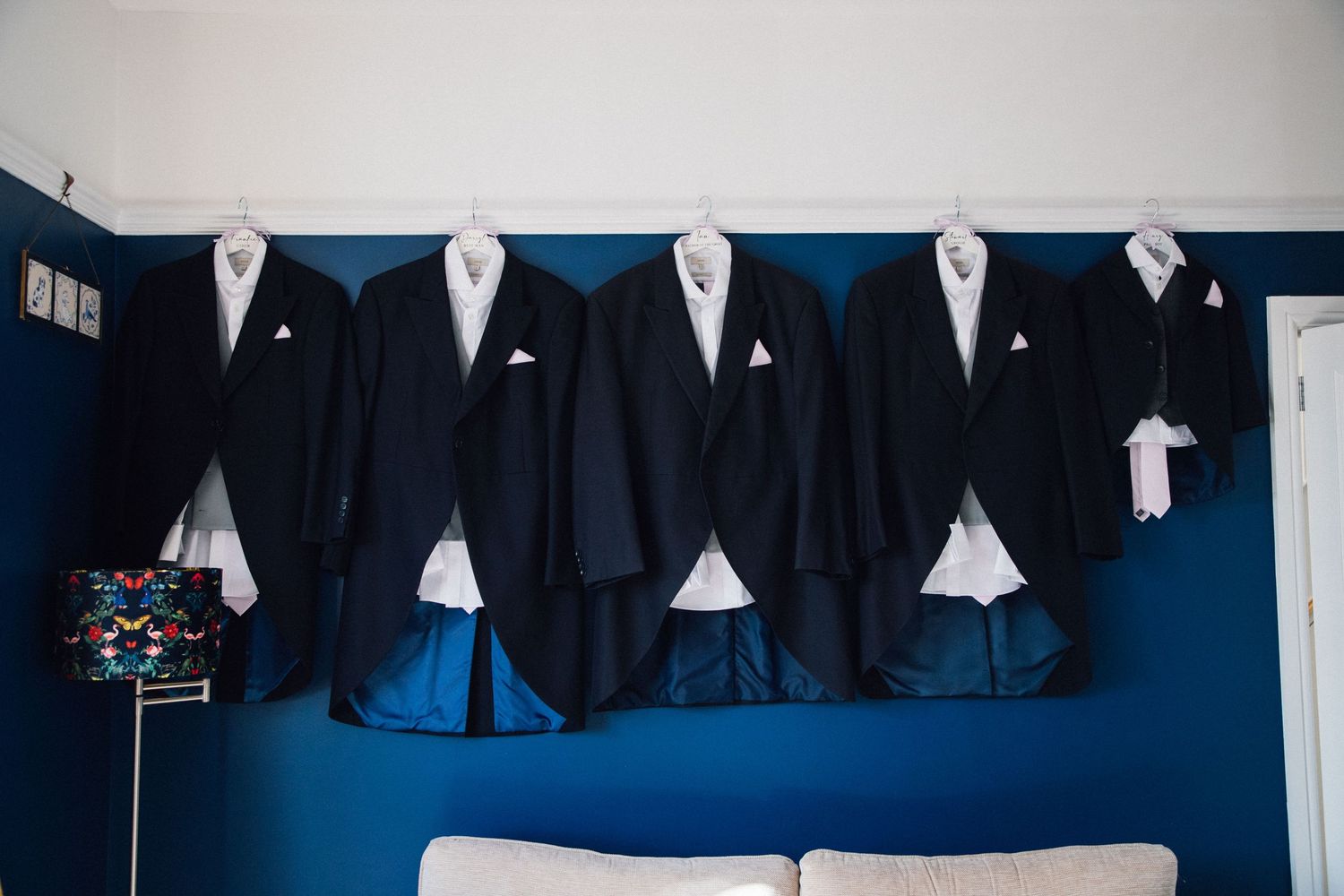 Black formal suits and dress shirts hanging in a row on hangers against a blue wall.