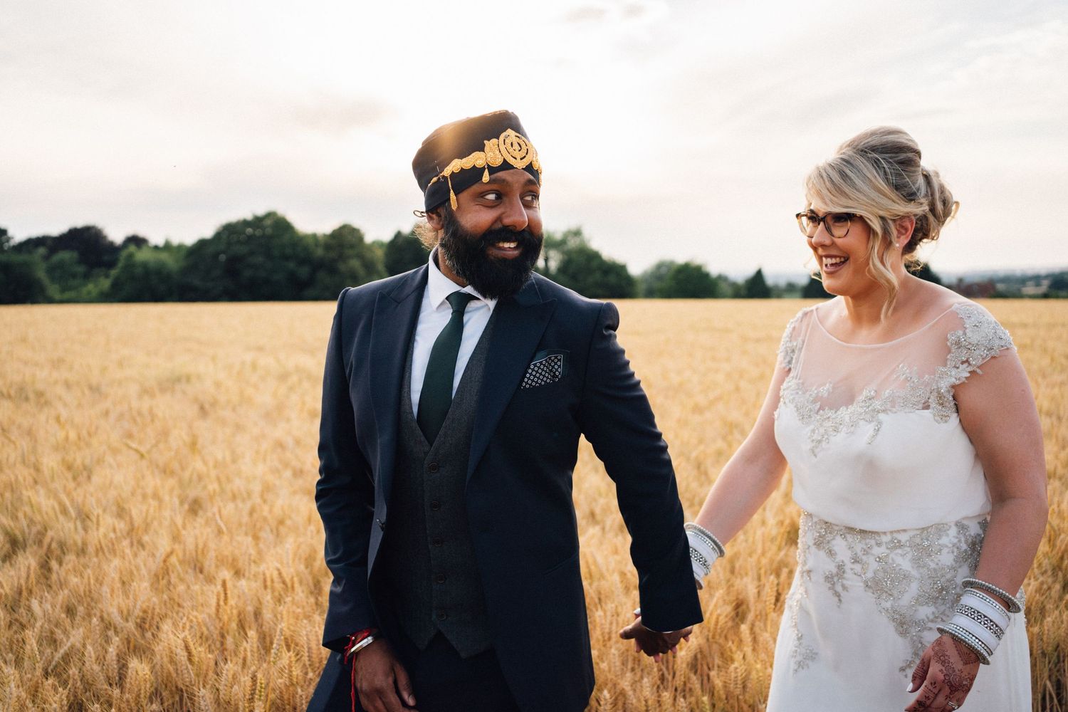 A couple in wedding attire holds hands while walking through a golden wheat field on their special day.