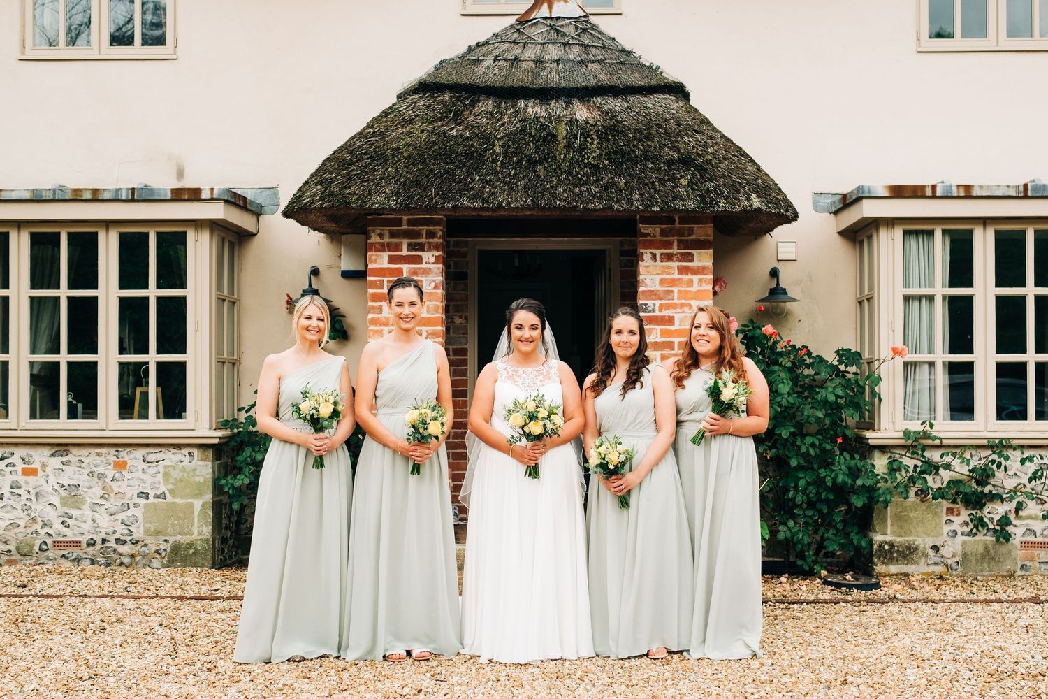 A wedding party poses in front of a charming thatched-roof country house entrance.