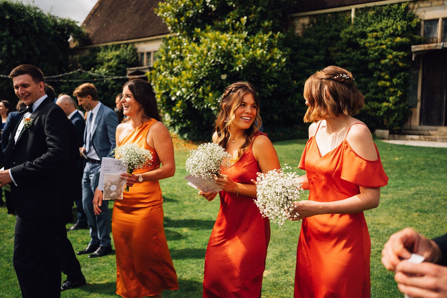Bridesmaids wearing vibrant orange dresses perform a choreographed dance routine at an outdoor reception.